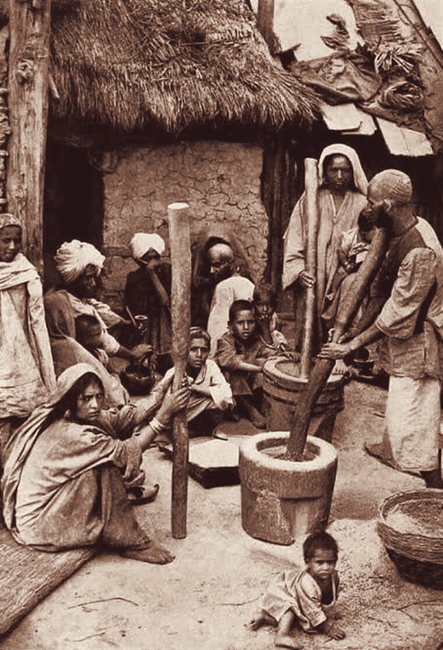 Archival photograph of a Kashmiri courtyard, family pounding grain with wooden pestles in a stone mortar